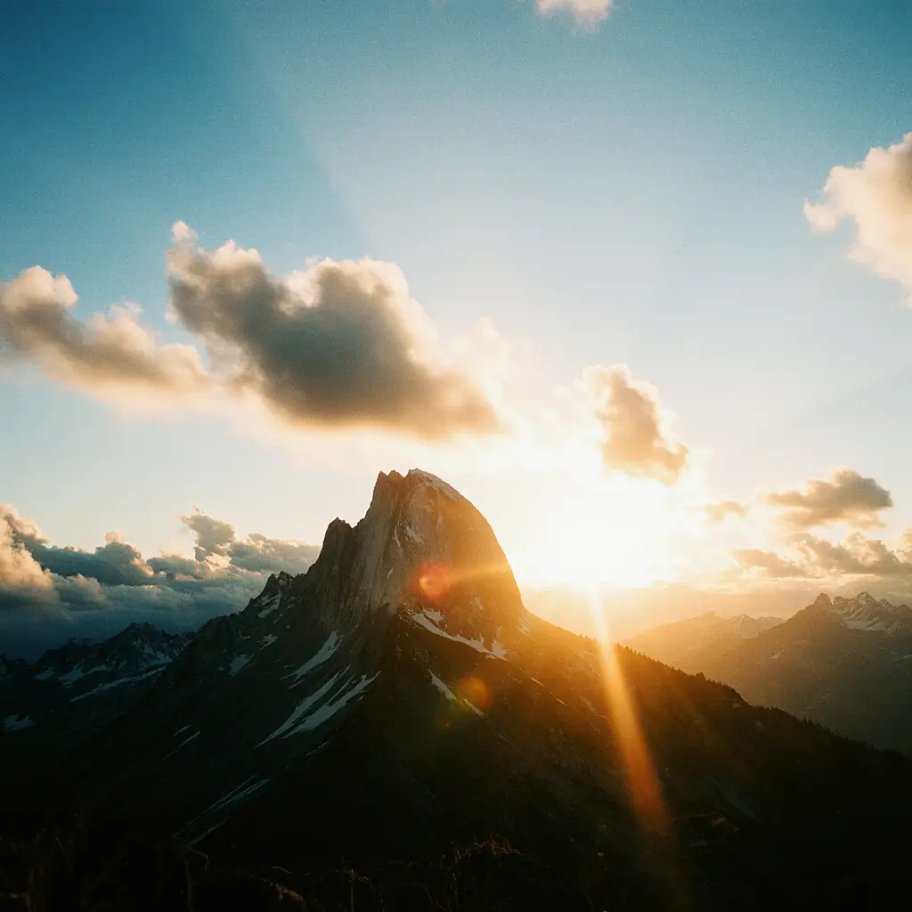 Dramatic mountain landscape at sunrise, with the sun’s rays breaking over a jagged peak partly covered in snow. Soft clouds catch the golden light, and distant mountain ridges fade into the horizon under a clear blue sky. Pixelated, with large square blocks obscuring details while the overall composition of sunlit clouds and silhouetted peak remains recognizable